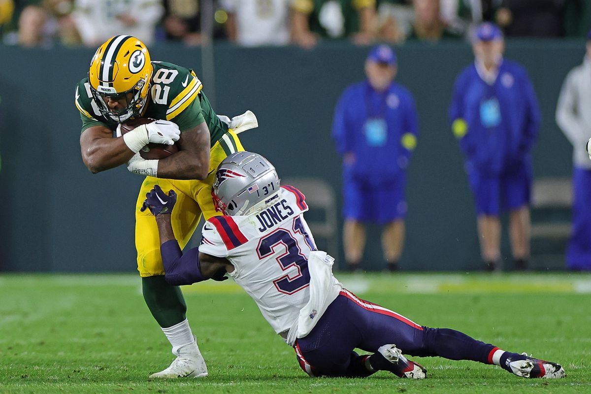 AJ Dillon of the Green Bay Packers is brought down by Jonathan Jones of the New England Patriots during a game at Lambeau Field on October 02, 2022 in Green Bay, Wisconsin. The Packers defeated the Patriots 27-24 in overtime.