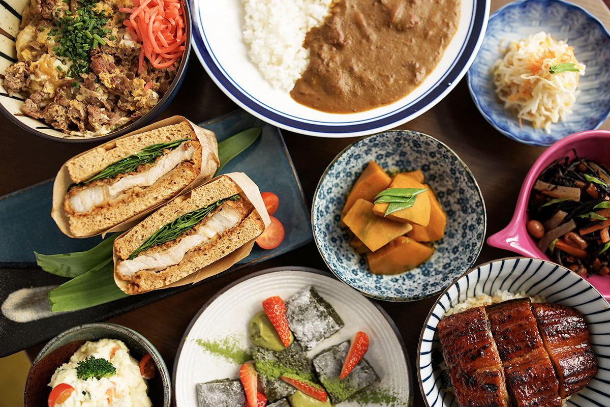 From above, a table full of dishes, including a katsu sandwich, curry with rice, pickled vegetables, eel, and topping-heavy rice bowl