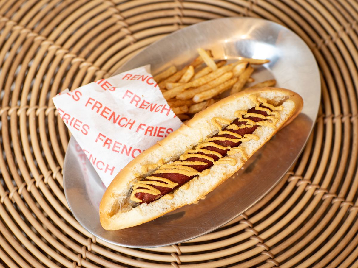 An overhead photograph of a thin sausage topped with mustard and accompanied by a side of french fries