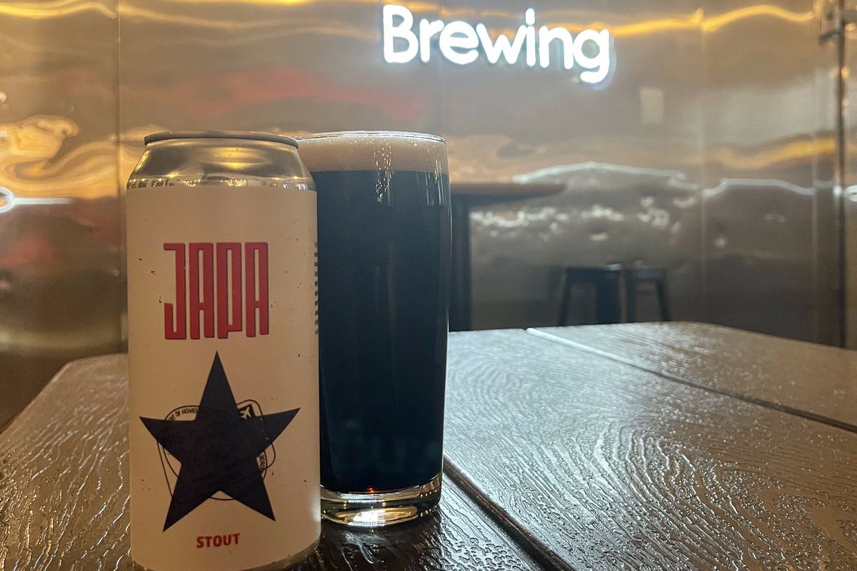 A can of Japa beer, with a star, next to a frothy draft in front of a neon Astral Brewing sign.