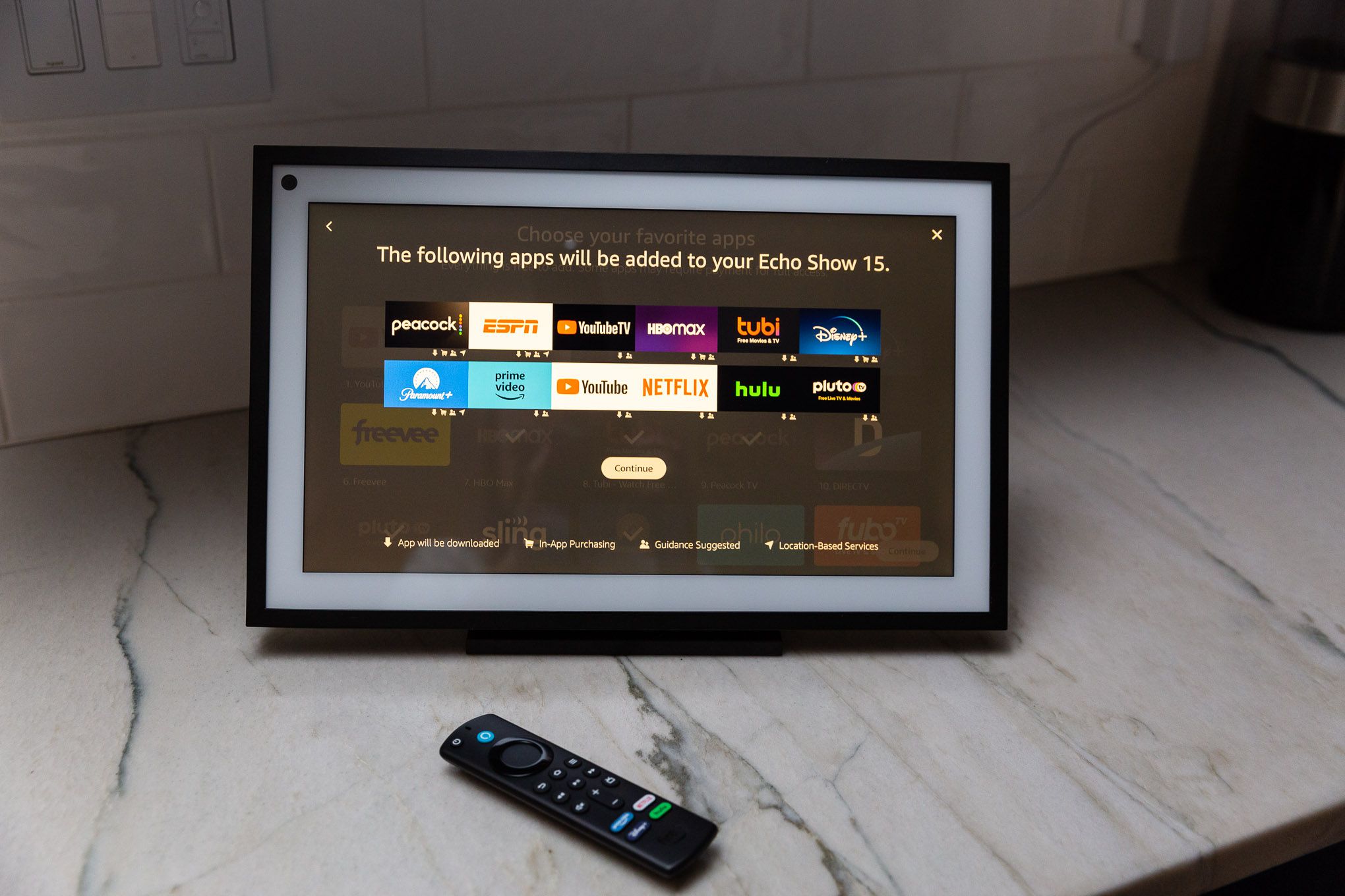 A Show 15 smart display on a kitchen counter with an Alexa remote control.