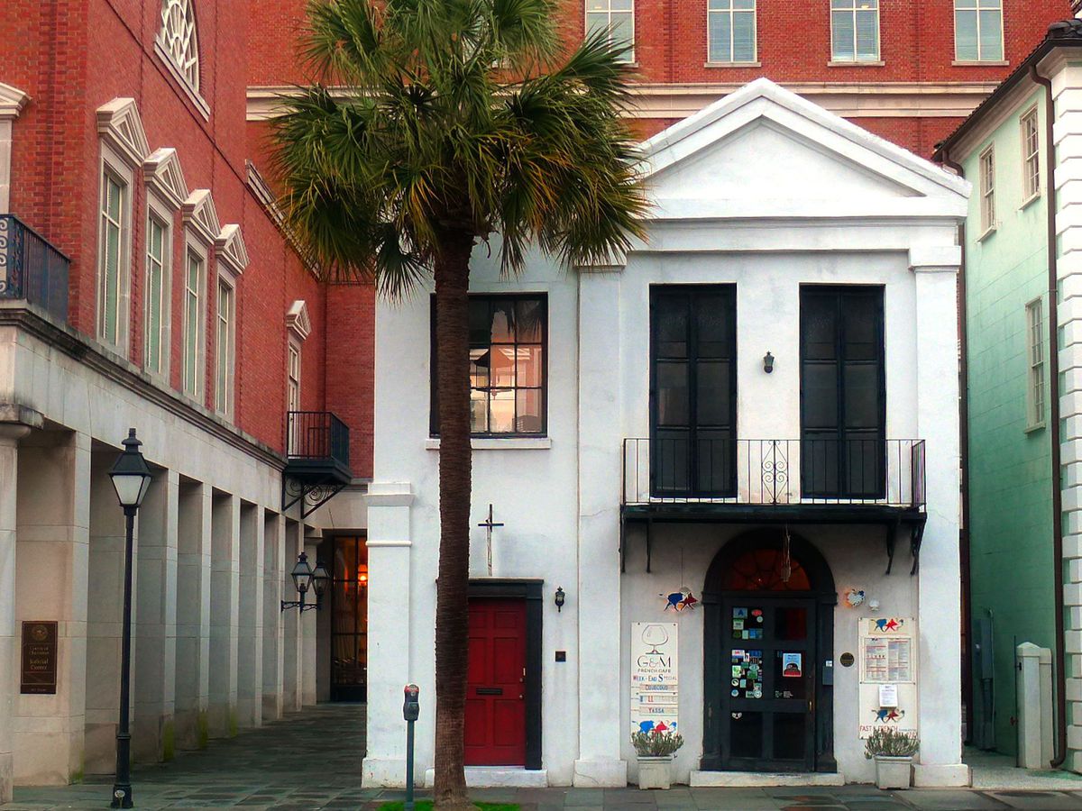A two-story white building with a palm tree in front. 