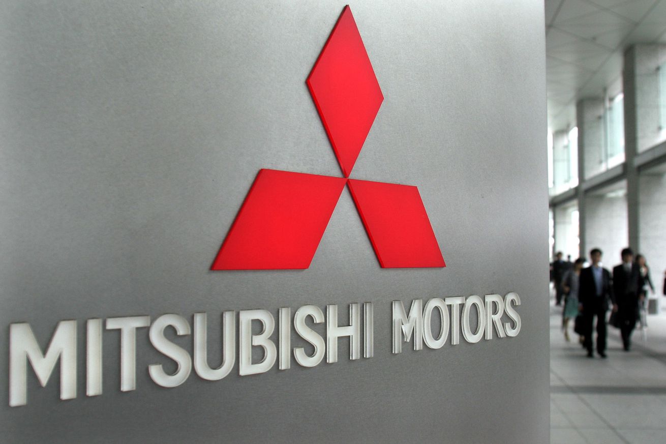 People walk past a silver wall with a red Mitsubishi logo on it.