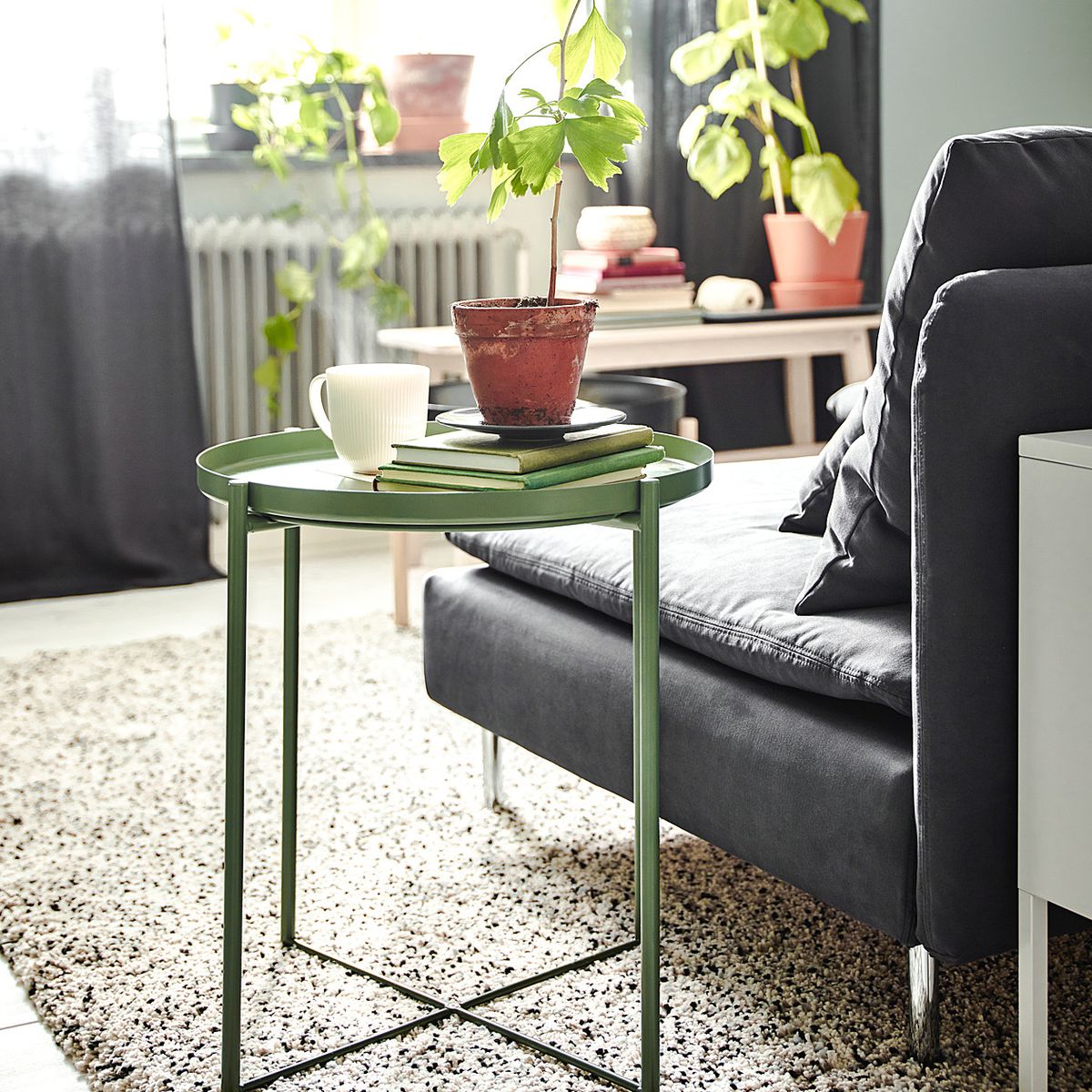 A green side table has books and a coffee mug on it and sits next to a couch. 