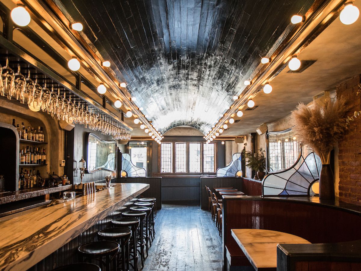 An ornate wine bar decorated with vintage light bulbs, a handsome marble countertop, and stained glass.