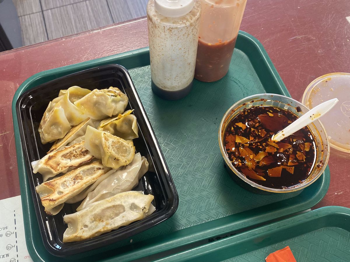 A black tray is filled with pumpkin and pork dumplings beside bottles of sauce.