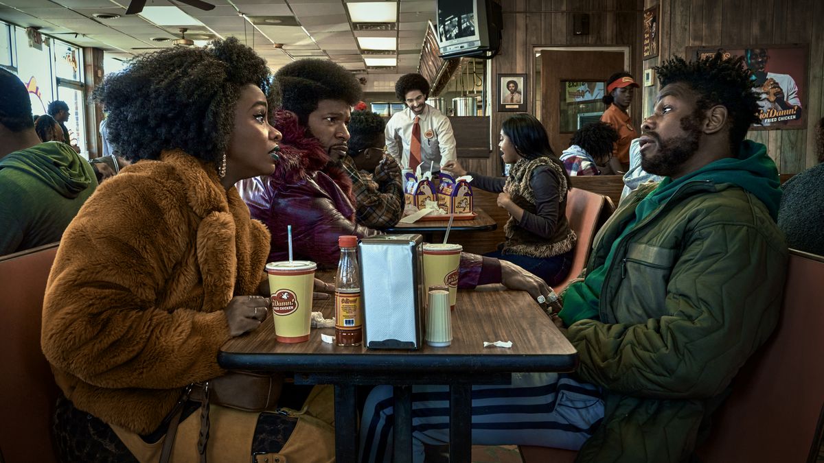 (L to R) Teyonah Parris as Yo-Yo, Jamie Foxx (Producer) as Slick Charles and John Boyega as Fontaine sitting across from one another at a fast food restaurant in They Cloned Tyrone.