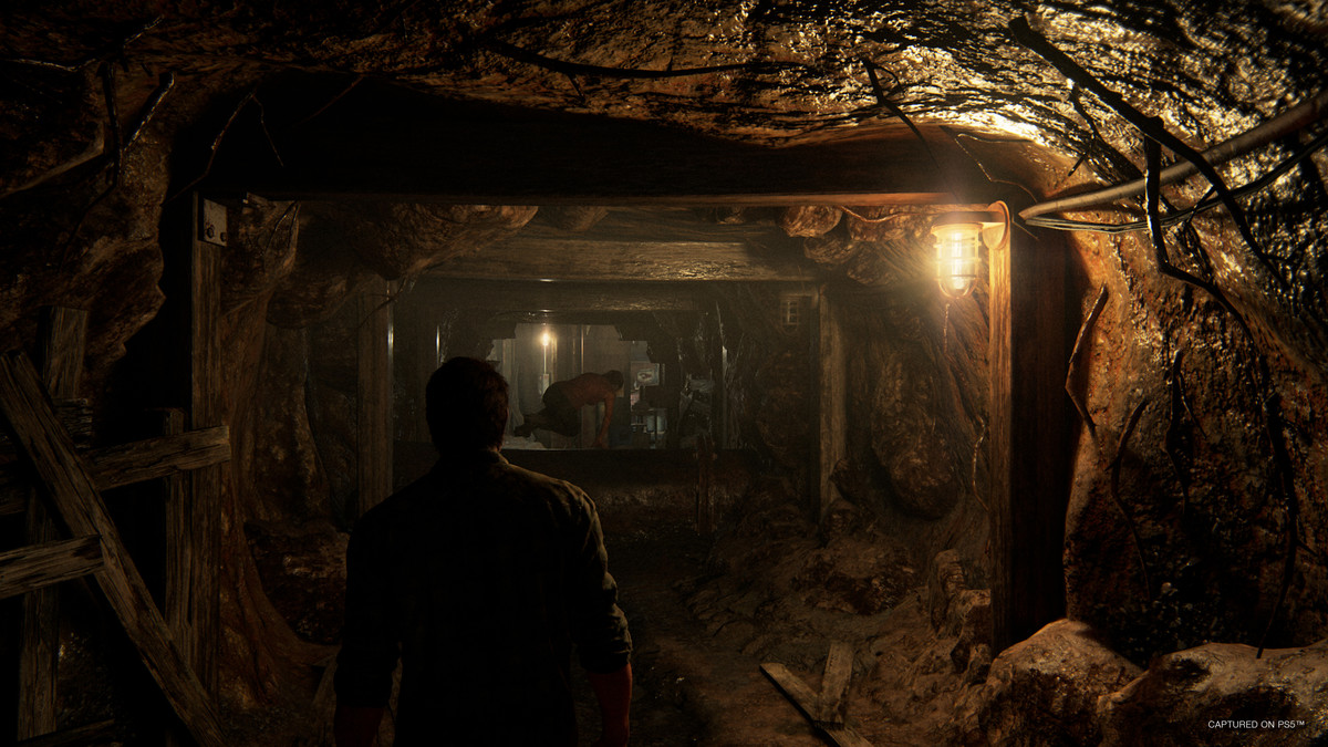 joel and ellie, from behind, in a dark cave