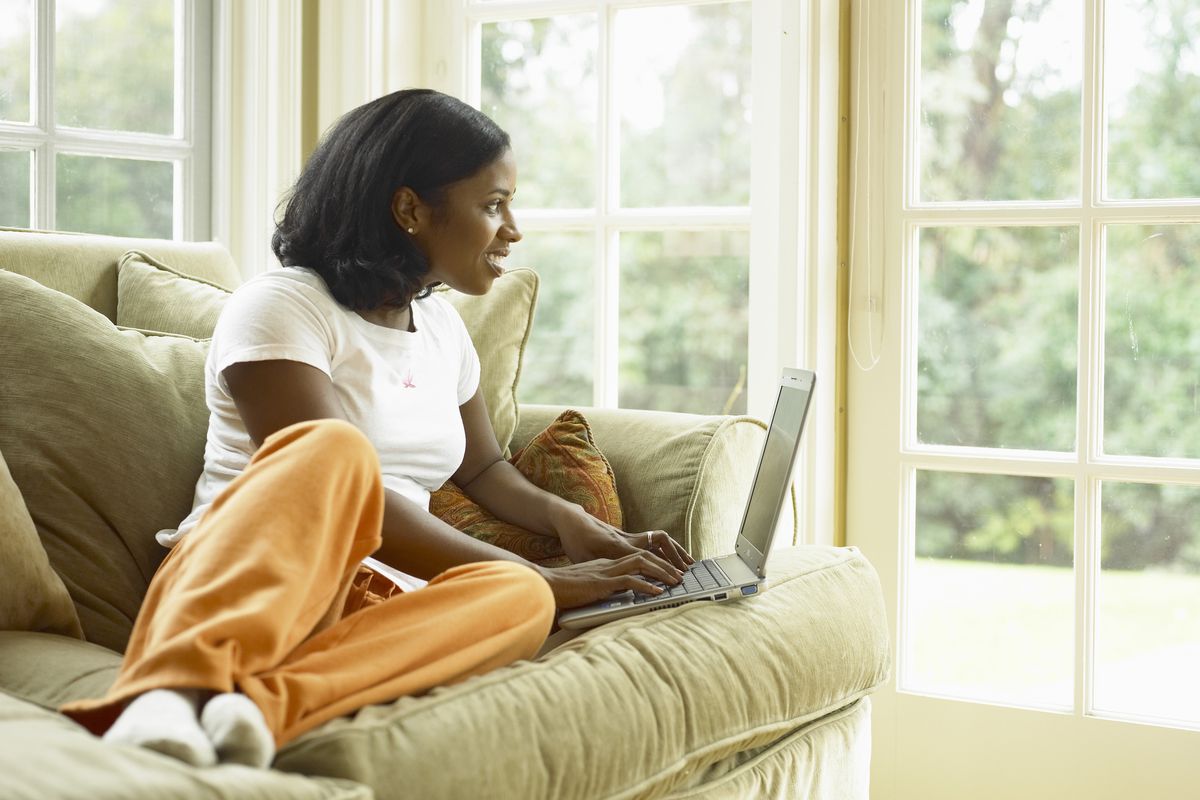 A woman wearing orange sweatpants, typing on a laptop on her couch