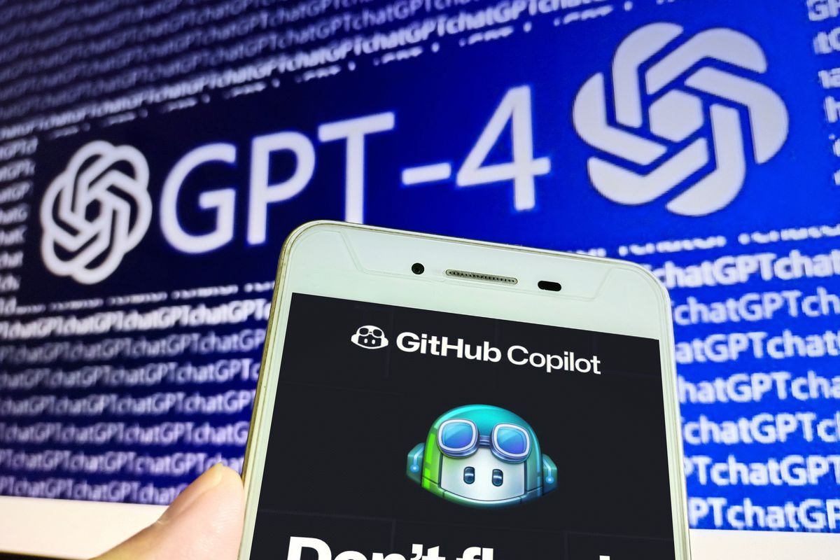 A smartphone screen shows GitHub’s Copilot tool, against a computer screen showing the AI GPT-4.