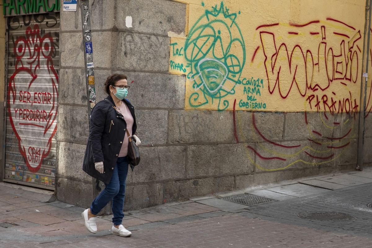 Woman in facemask walking past graffitied wall in Madrid
