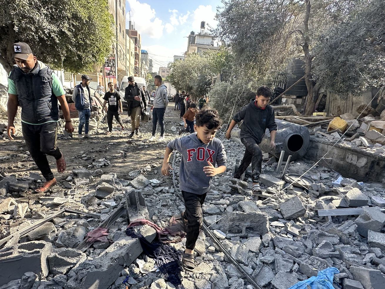 People walking through bombed building rubble looking for survivors.