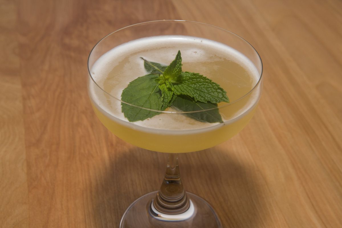 A yellow cocktail with a big green leaf in stemmed glass.