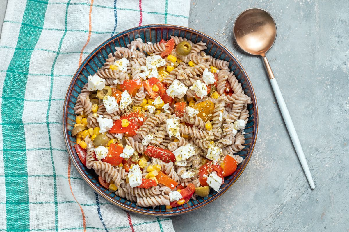 A bowl of pasta salad featuring fusilli with corn, tomatoes, and feta cheese.