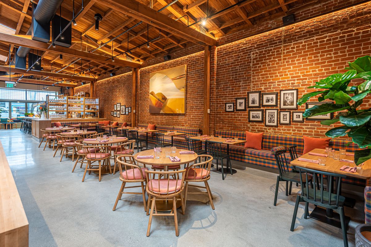 Round four-top tables and brick walls inside a new restaurant with tall ceilings.