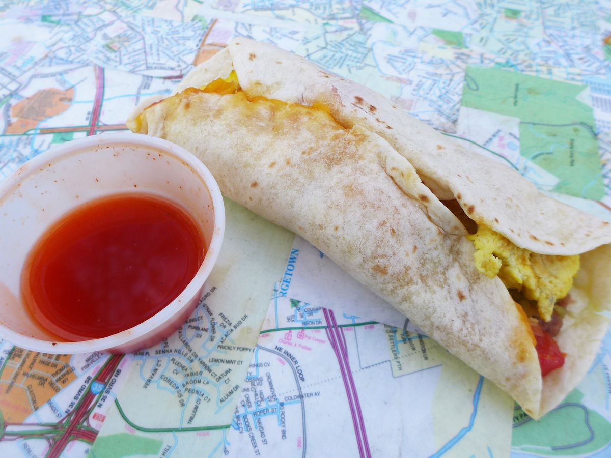 A flour tortilla taco with egg inside and red salsa on the side, on a street map of Austin.