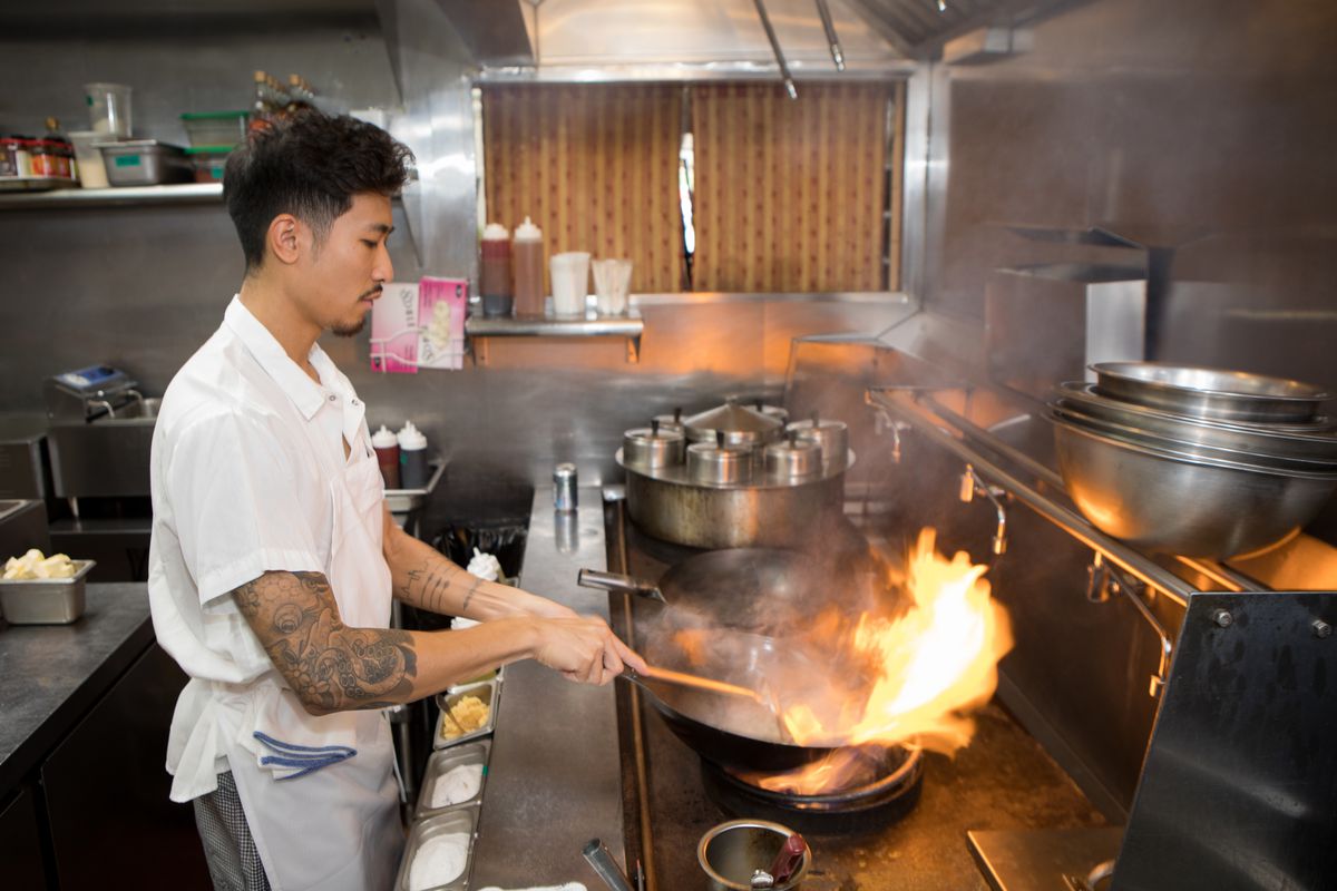 Calvin Eng stirs a flaming wok in the Win Son kitchen,