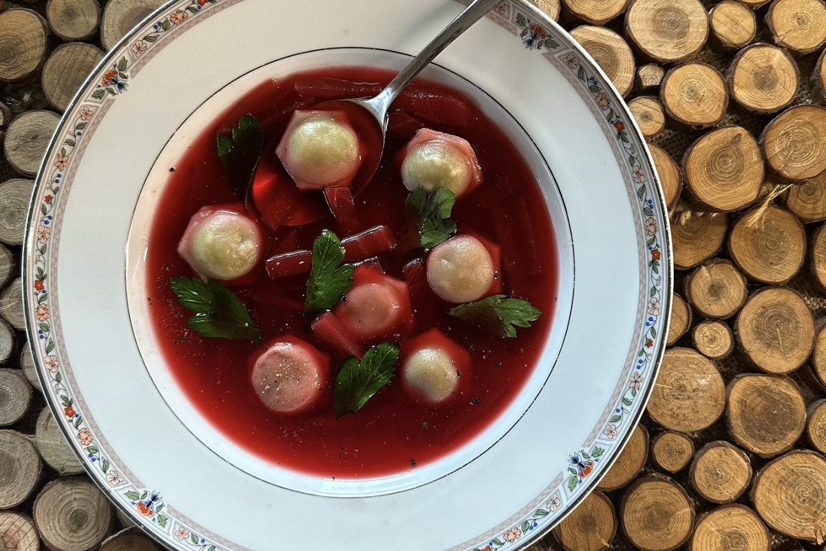 Bright red borscht with dumplings and parsley in a shallow white bowl.