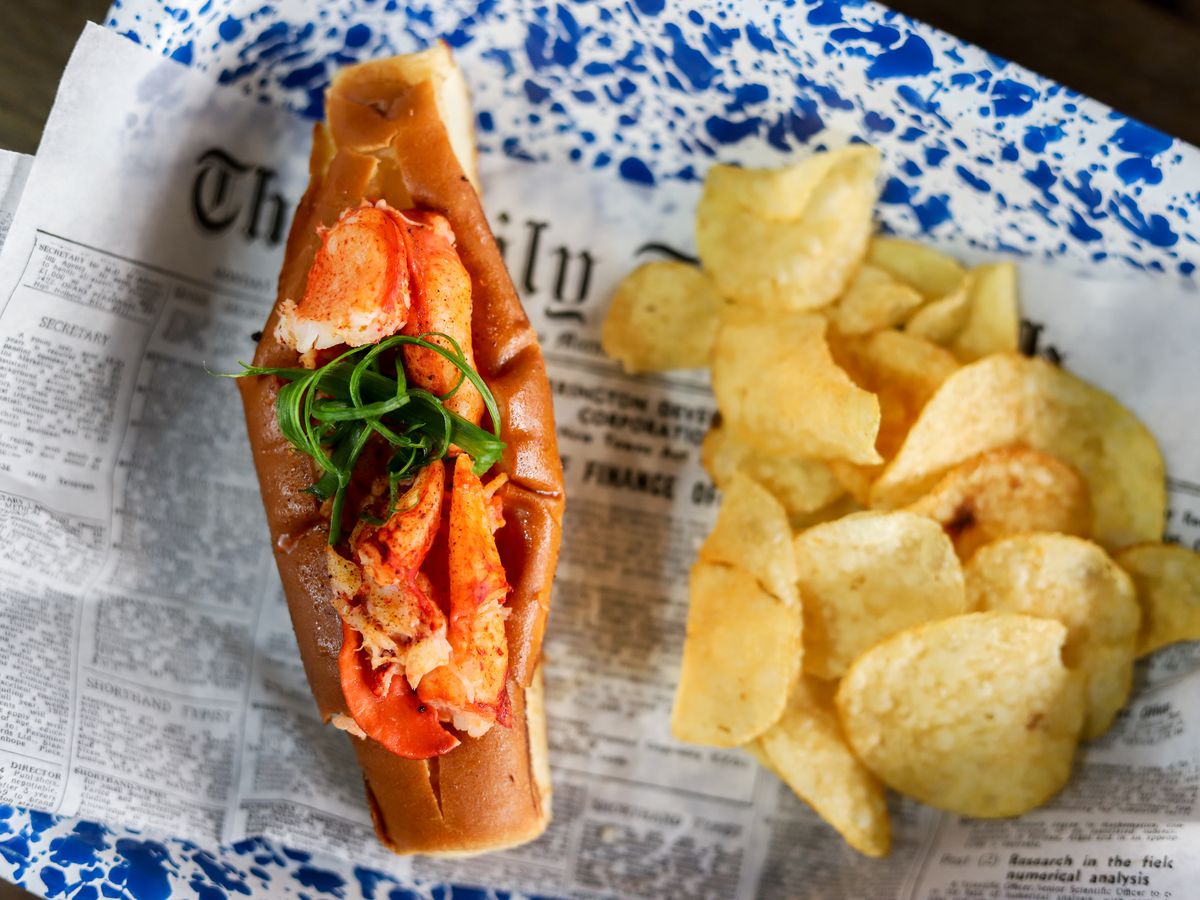 Lobster roll and potato chips on newspaper on a blue patterned plate