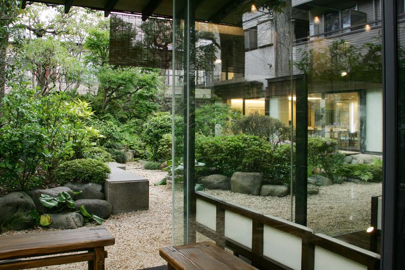 A lush garden with large stones and benches, butting against a glass wall.