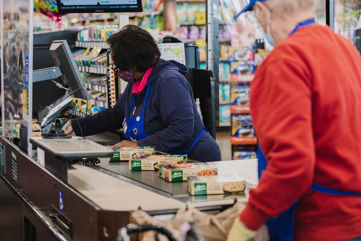 A cashier at a grocery store scans items on a conveyor.