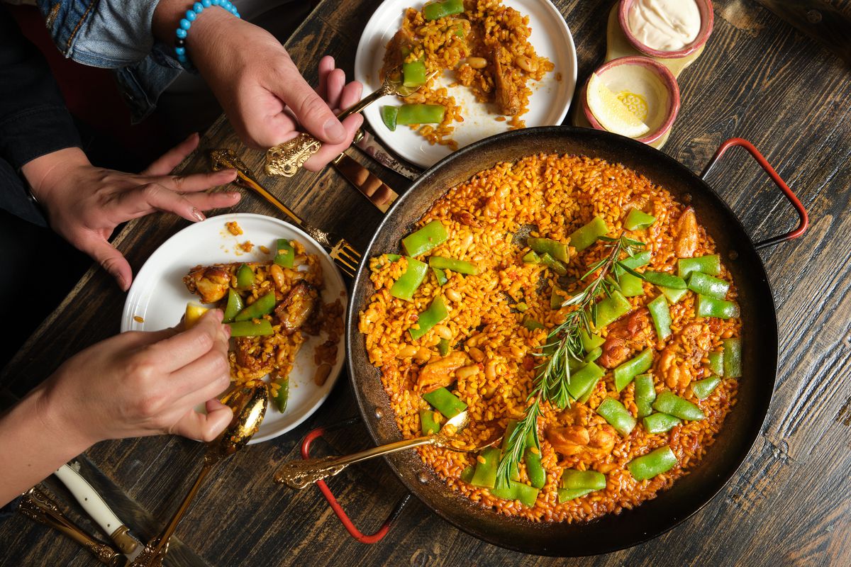 A pan of paella with hands in the photo