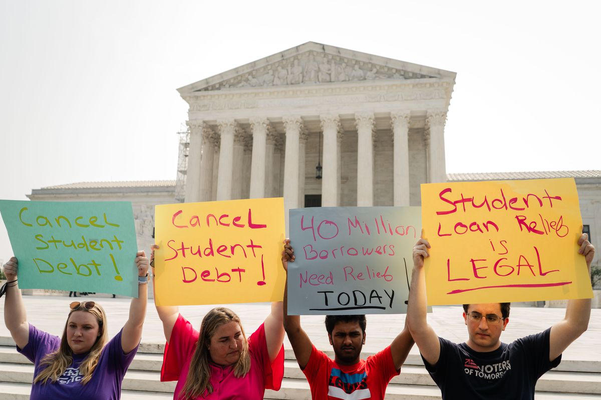 Protesters in front of the Supreme Court building hold signs reading, “Student loan relief is legal” and “Cancel student debt.”