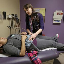 In this March 28, 2013 photo, medical resident Stephanie Place examines Maria Cazho at the Erie Family Health Center, in Chicago. As clinics gear up for the expansion of health insurance, they're recruiting young doctors. 