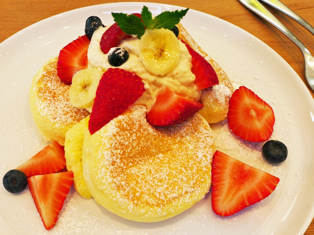 Three thick pancakes covered with powdered sugar and assorted fruit.