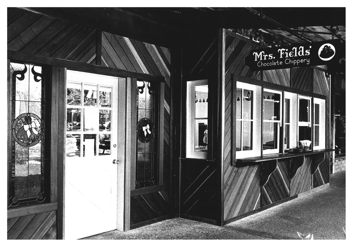 Black and white photo of a shop exterior with a sign reading “Mrs. Fields’ Chocolate Company.”