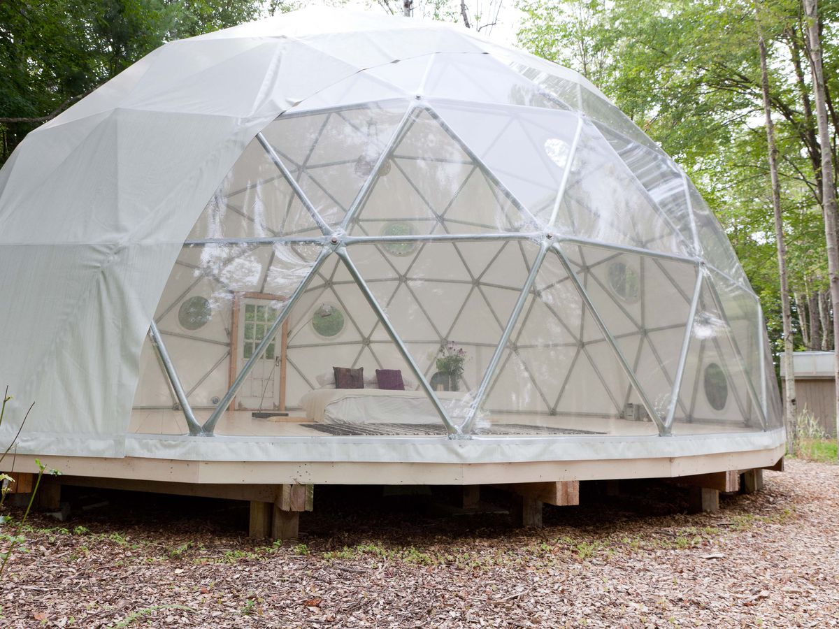 A dome-shaped tent sits on a wooden platform in the middle of a clearing in a forest. 