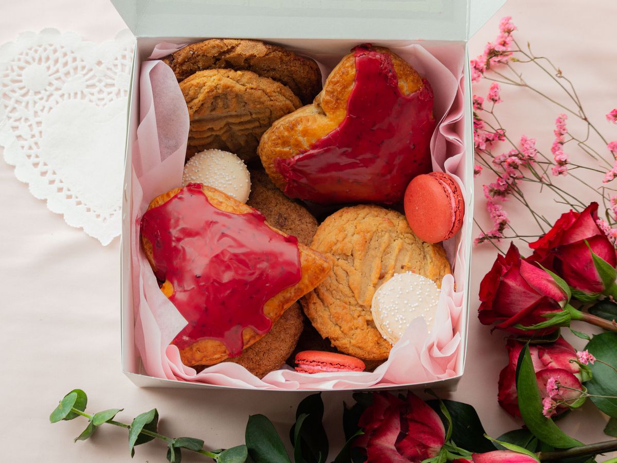 On a pink cloth with roses, a box is filled with heart-shaped and round cookies for Valentine’s Day. 