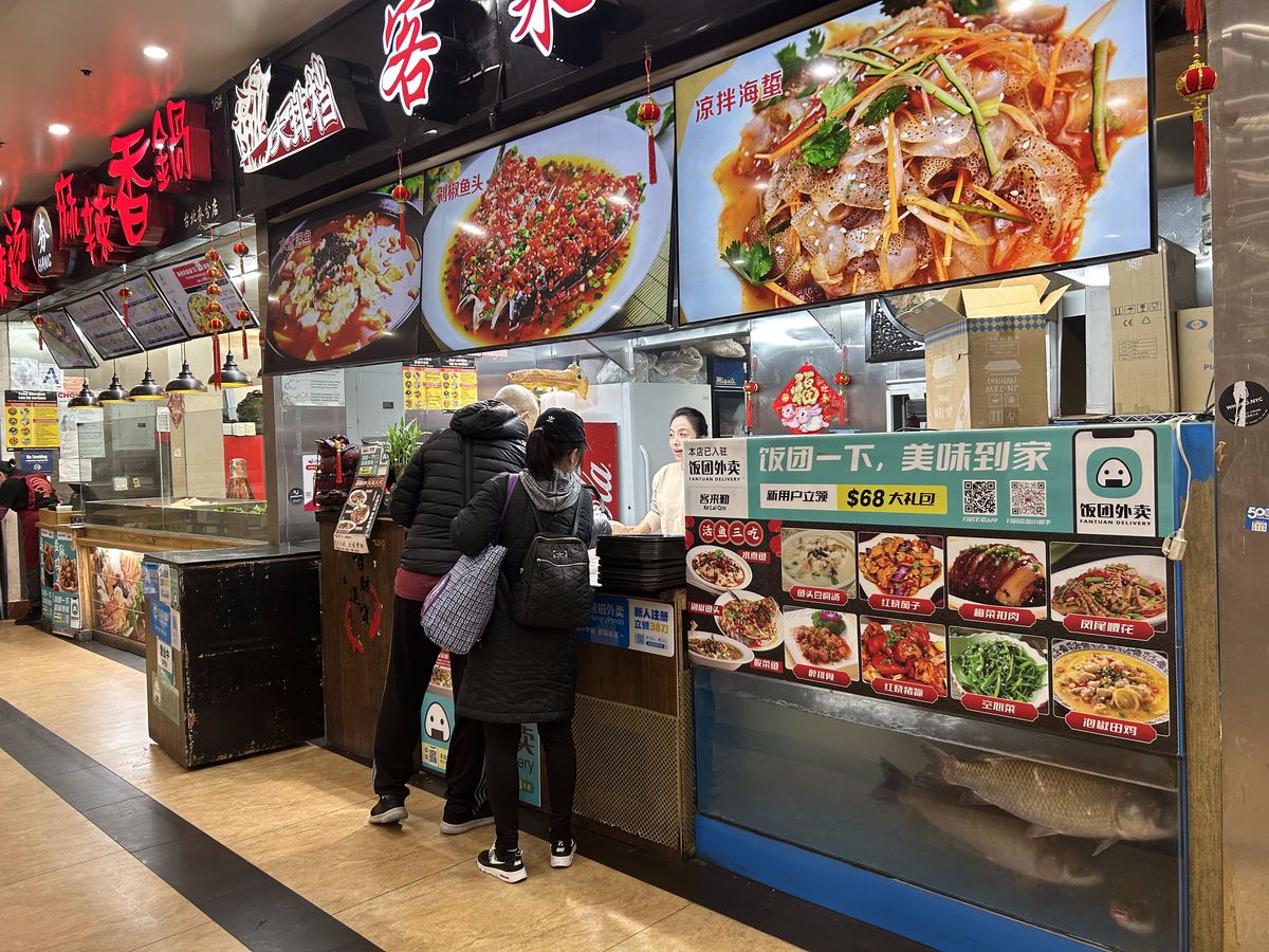 Customers stand at the counter of a restaurant whose name and menu items are listed in Chinese.