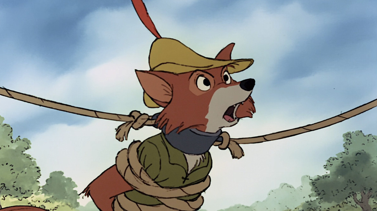 Disney’s Robin Hood, an anthropomorphic fox in green, stands looking angry with ropes wrapped around his body and a metal collar around his neck in the 1973 animated movie