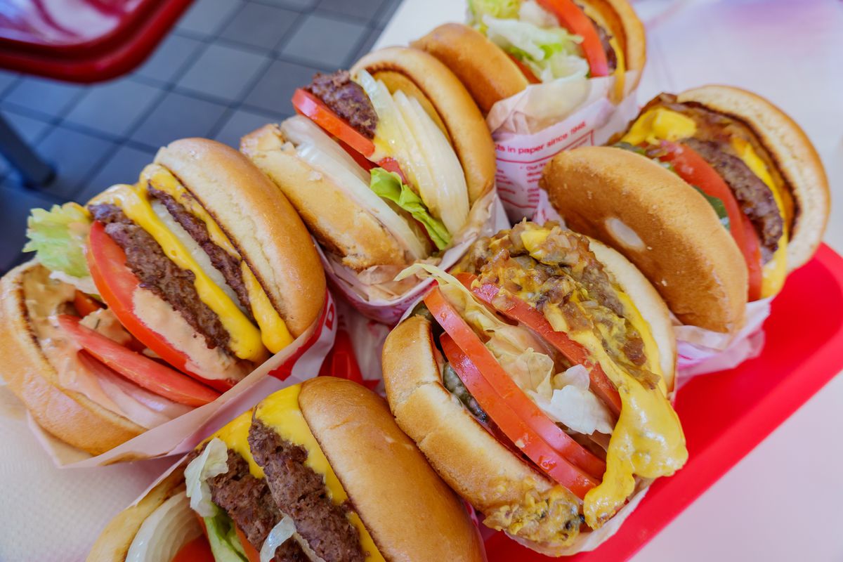 A picture of six In-N-Out burgers on a red tray with lettuce, tomato, cheese, and onions