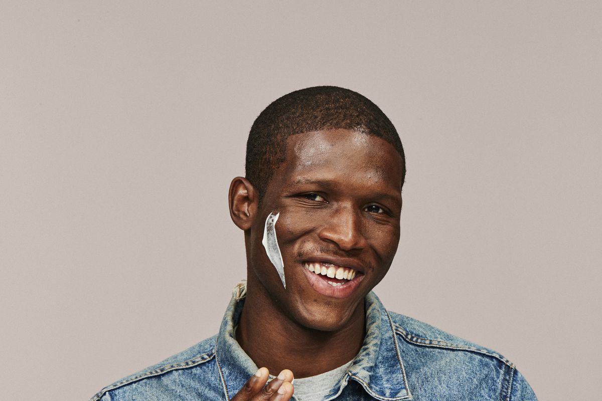 A man smiles, with a swipe of lotion on his face.