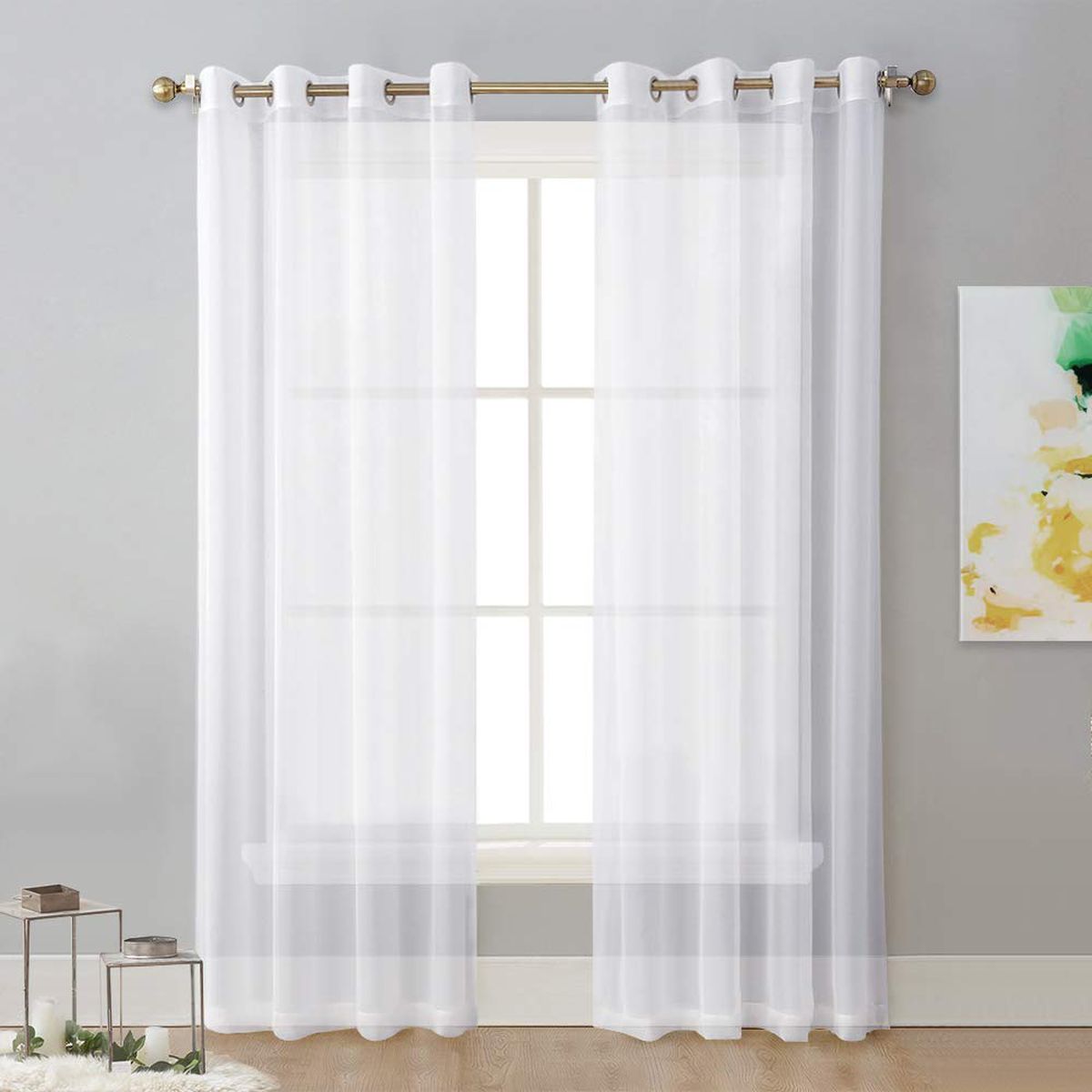 Sheer white curtains hang on a white window. The walls are gray and they feature white trim. 