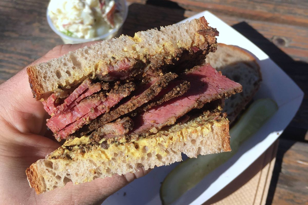 A hand holding up a pastrami sandwich. 