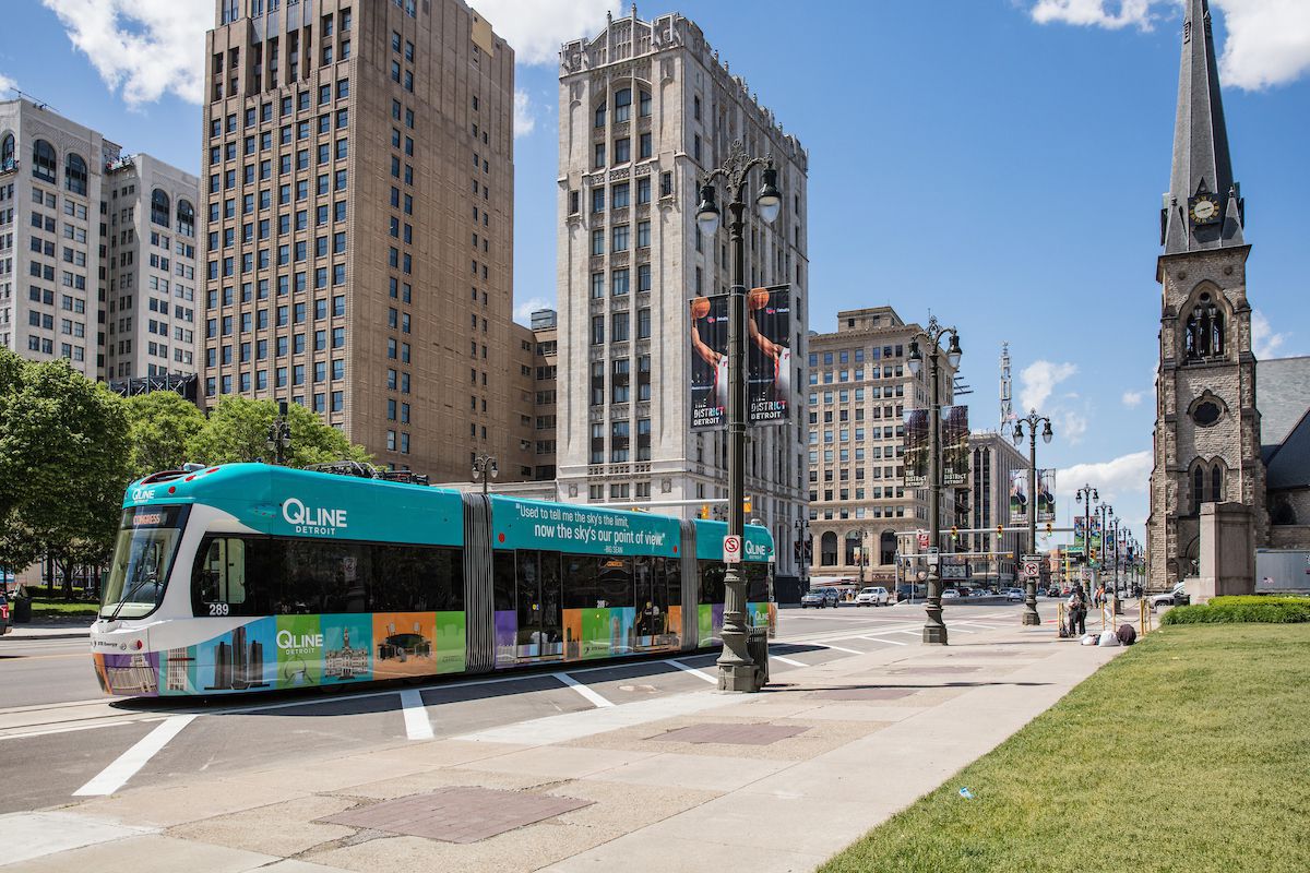 A street in Detroit. There is a bus that has a sign that reads: Q Line. There are buildings on both sides of the street.