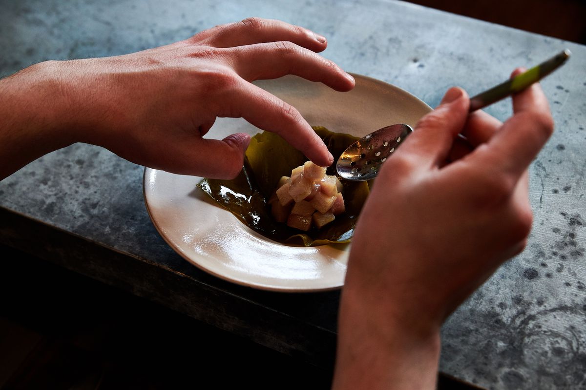 Two hands delicately plate a seafood dish in a bowl at Erizo