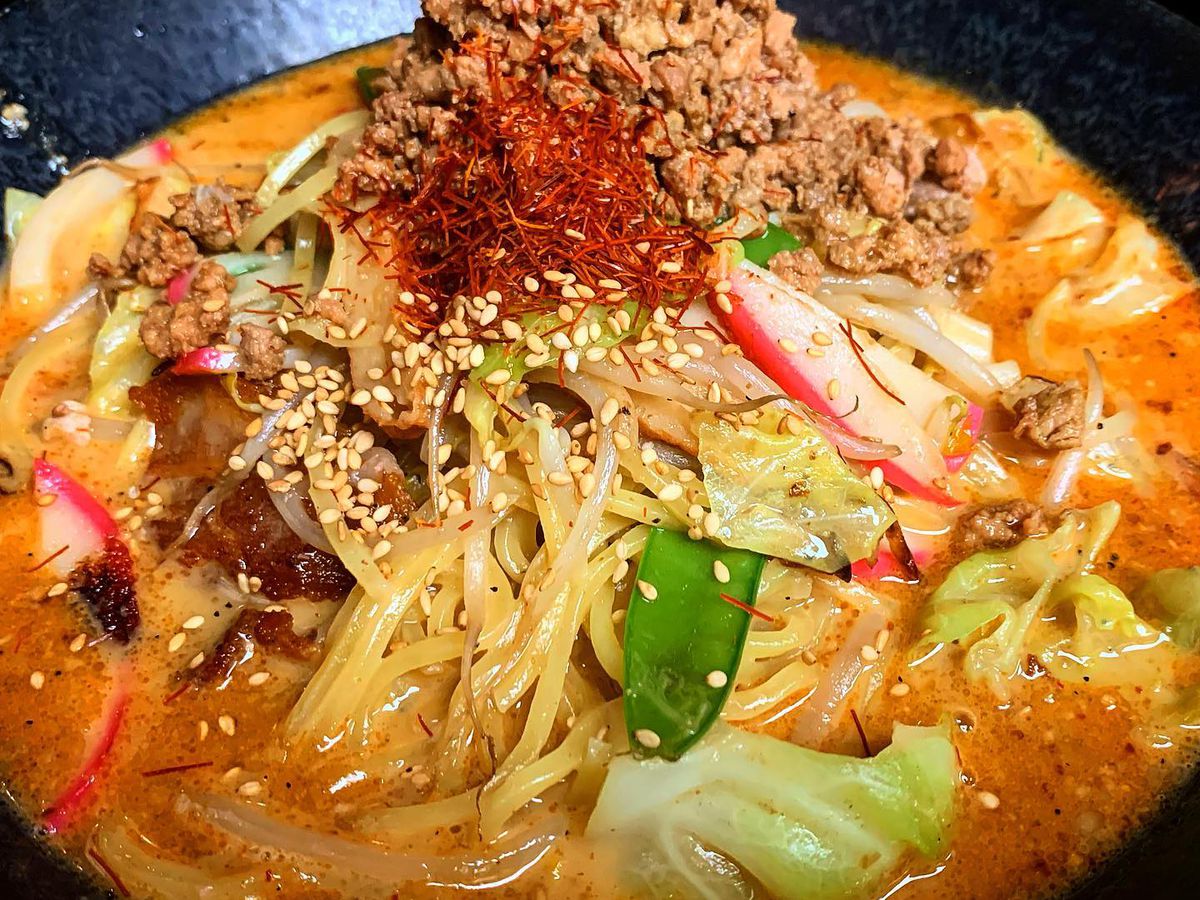 Closeup on a bowl of bright yellow-orange broth topped with ground pork, sesame seeds, bok choy, and more.