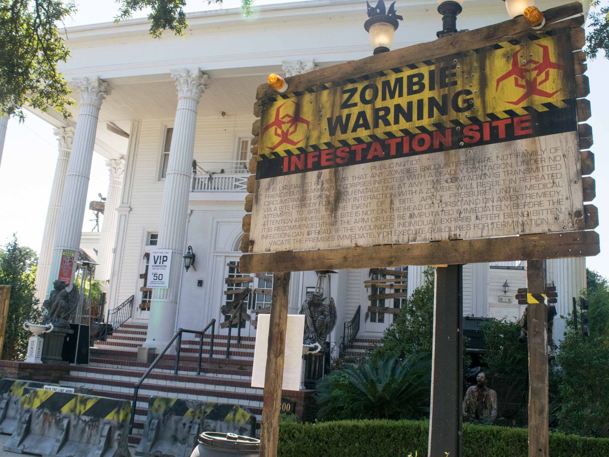A large white building with columns. In front of the building is a sign with words that read: Zombie Warning Infestation Site.