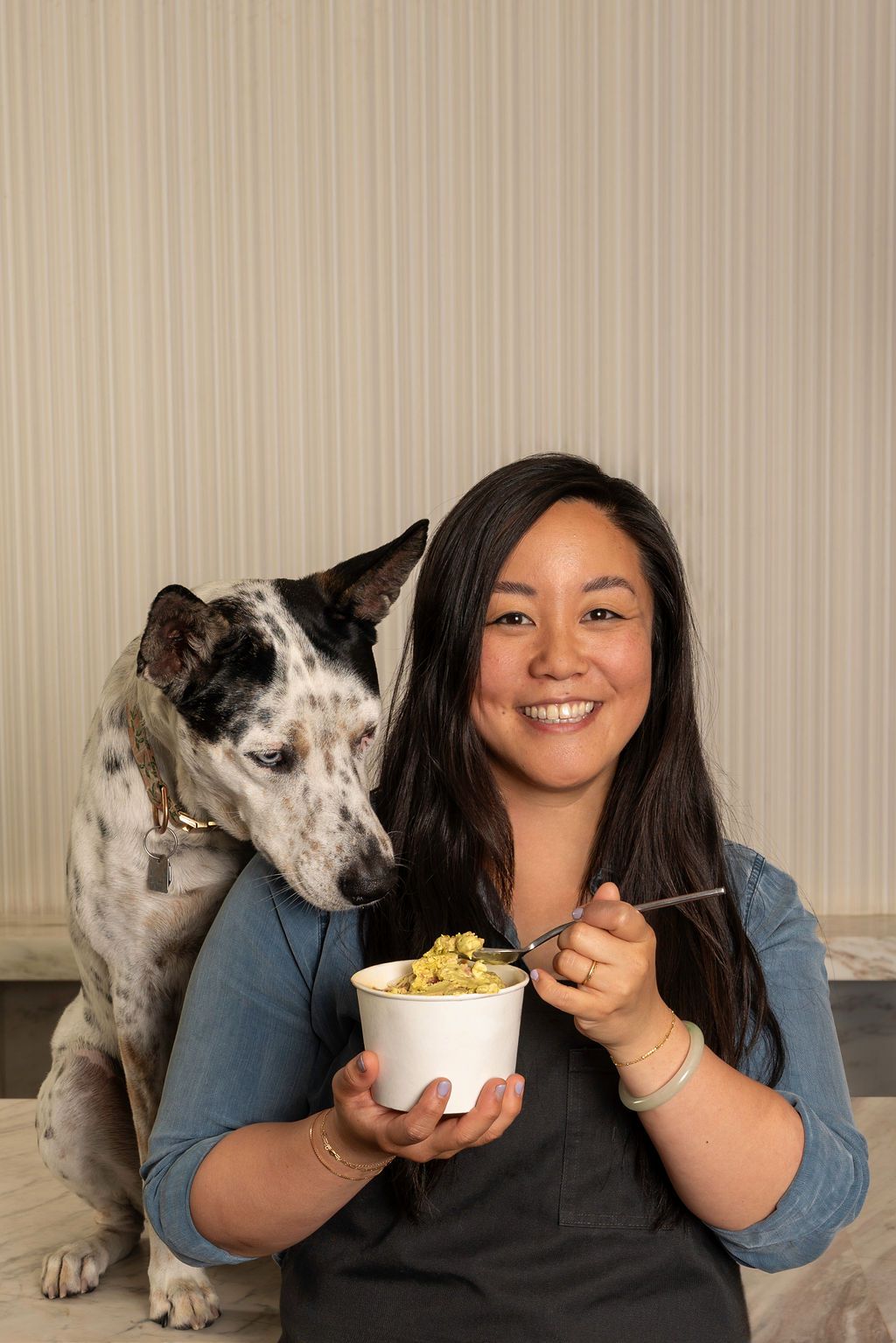 A woman holds ice cream and a dog looks over her shoulder.