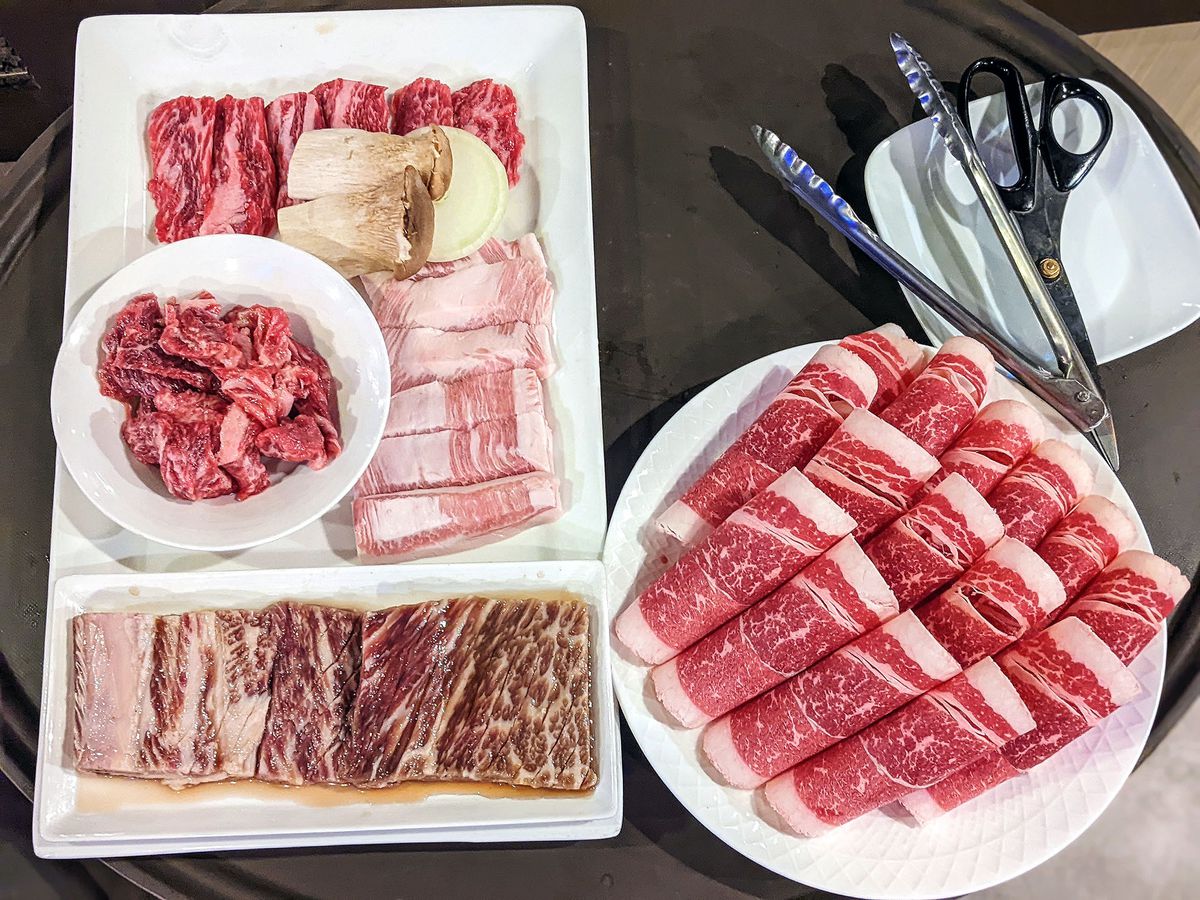 Raw sliced meats on white platters with metal tongs.