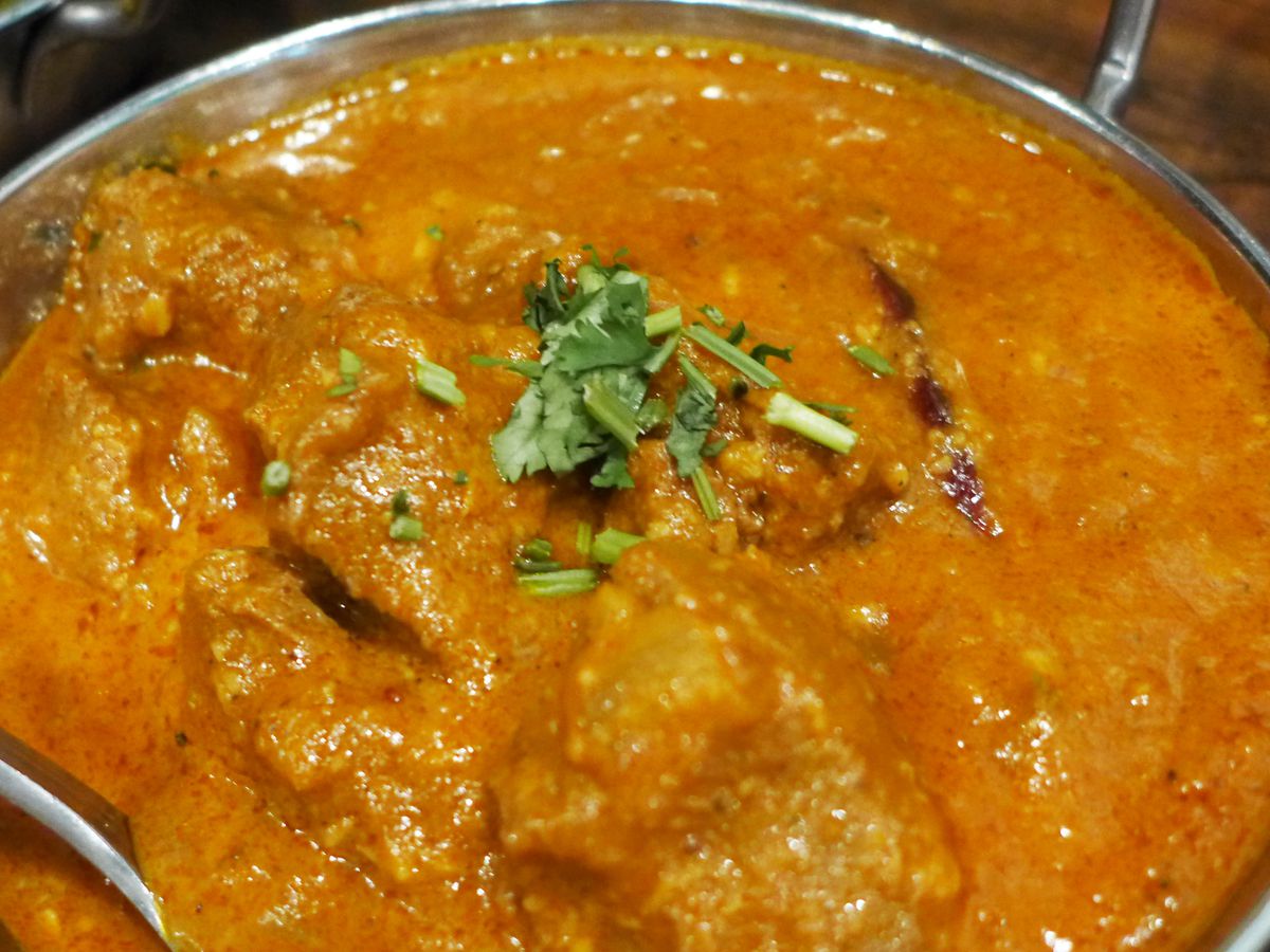 A chicken curry in a metal bowl with a yellowish cast.