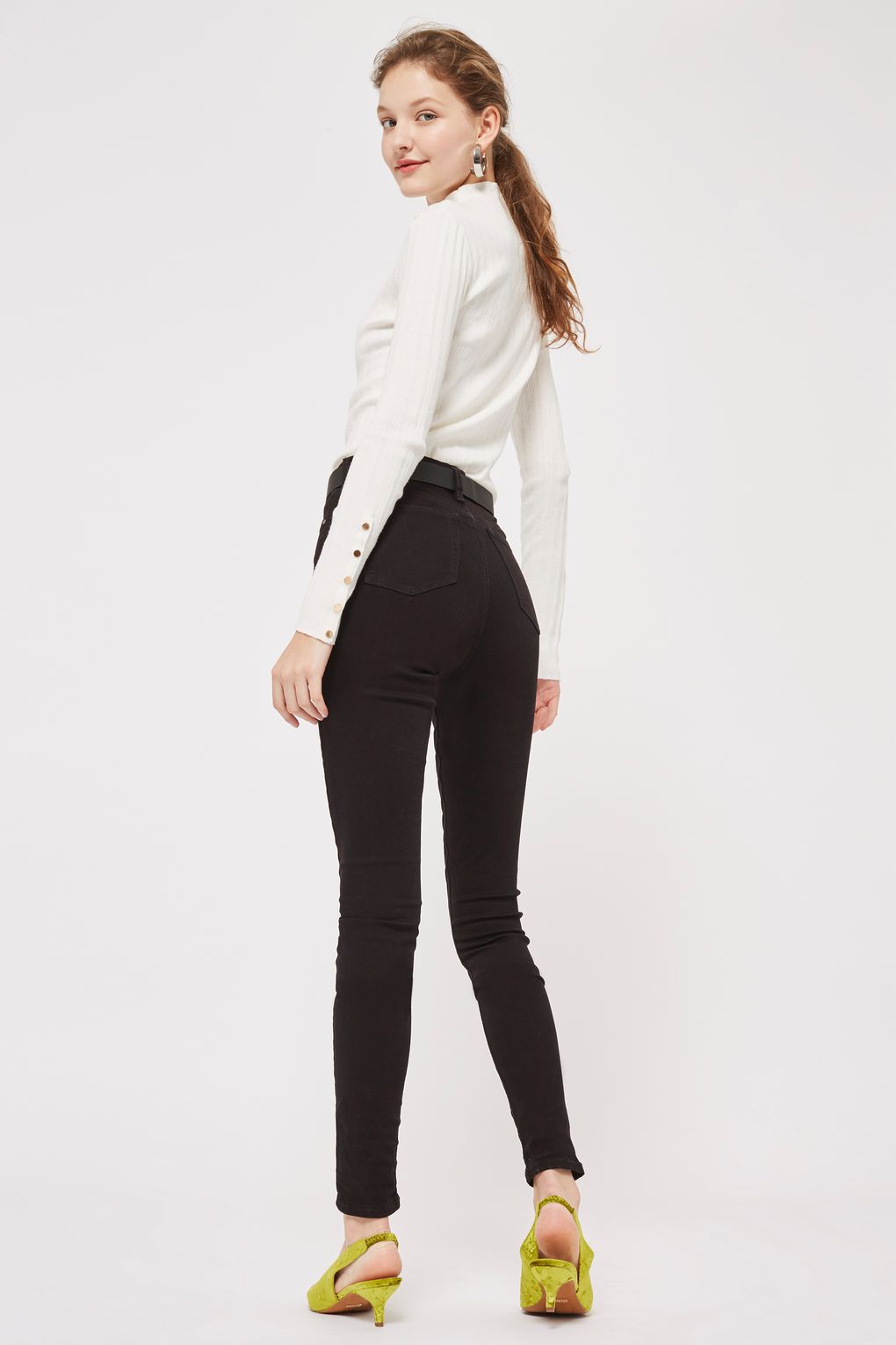 A model wearing black skinny jeans and a white turtleneck