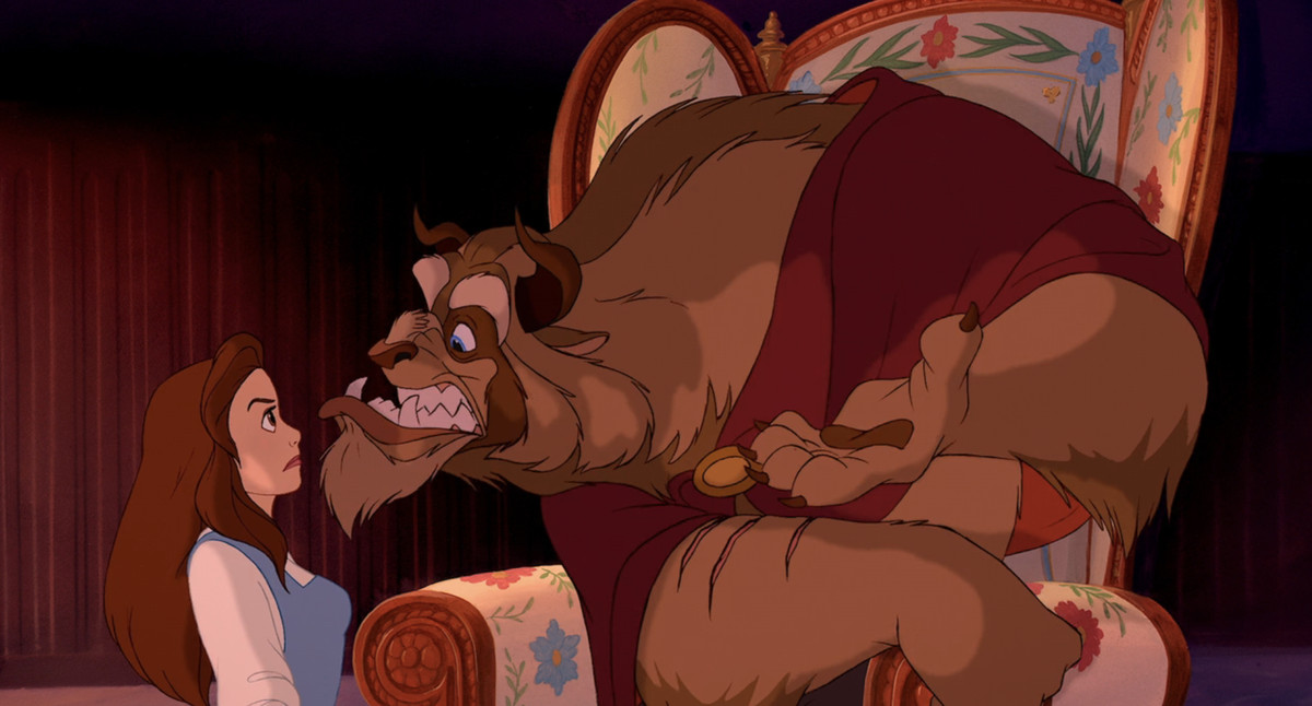 Beast, a huge furry creature with small ram horns, wearing a red cloak, snarls at a defiant Belle in Disney’s Beauty and the Beast