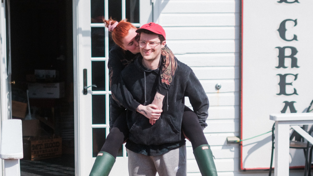 A man holds a woman in a piggyback in front of an ice cream shop.