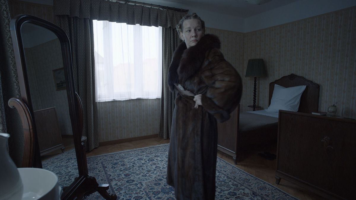 Sandra Huller as Hedwig Höss in The Zone of Interest, looking in a mirror while wearing a fur coat