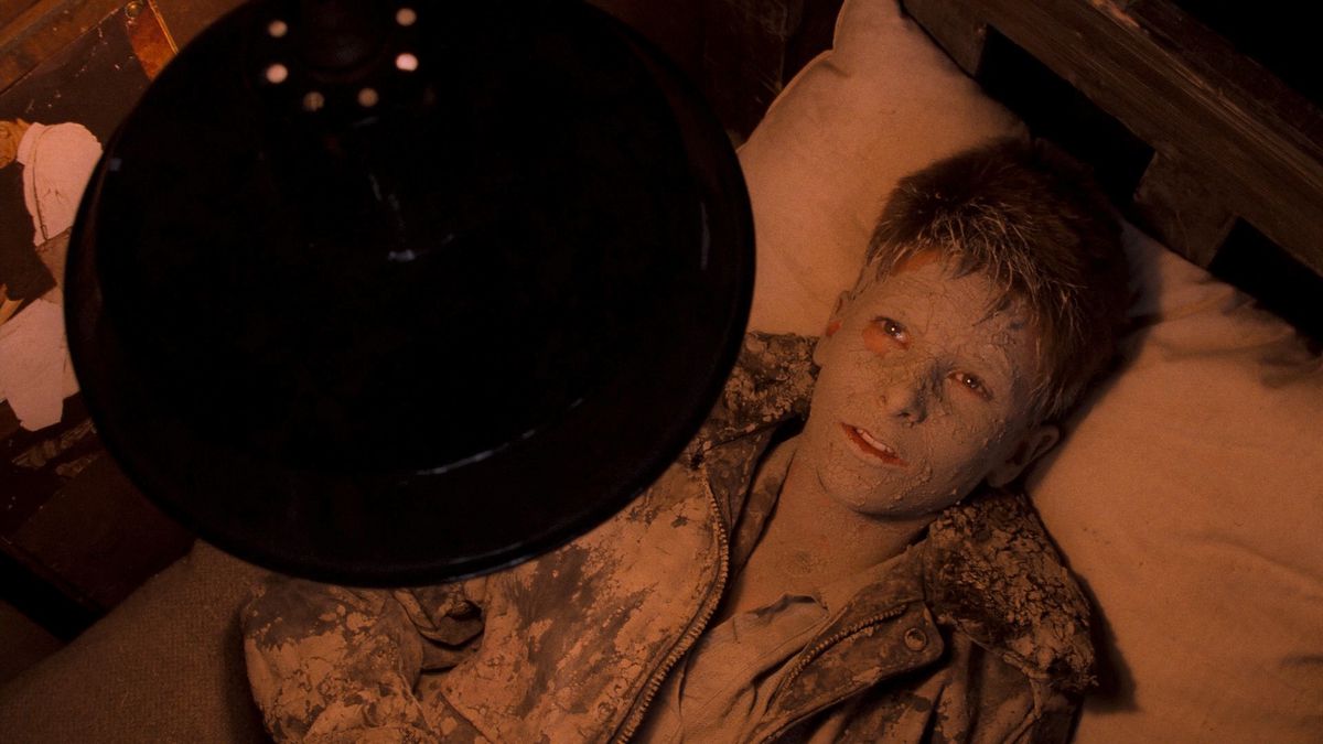 Jamie (a young Christian Bale)sits caked in mud on a bed staring at the ceiling in Empire of the Sun